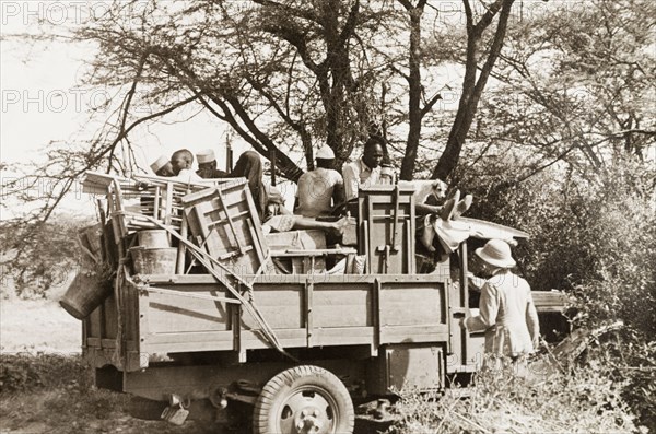 Jeep made ready for safari. African porters sit amongst a jumble of folding tables and chairs in the back of a jeep, waiting to leave on safari. Kenya, circa 1935. Kenya, Eastern Africa, Africa.