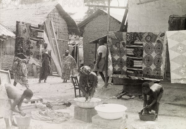 Washing day at an Asante village. Women and children wash clothes outdoors at an Asante (Ashanti) village. Large squares of patterned cloth are hung up to dry on a washing line behind them. Western Asante, Gold Coast (Ghana), circa 1950., Ashanti, Ghana, Western Africa, Africa.