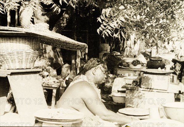 Market stall in Accra. A Ghanaian woman sits at her stall at a marketplace in Accra, selling a variety of cooking utensils and wicker goods. Accra, Gold Coast (Ghana), circa 1950. Accra, East (Ghana), Ghana, Western Africa, Africa.