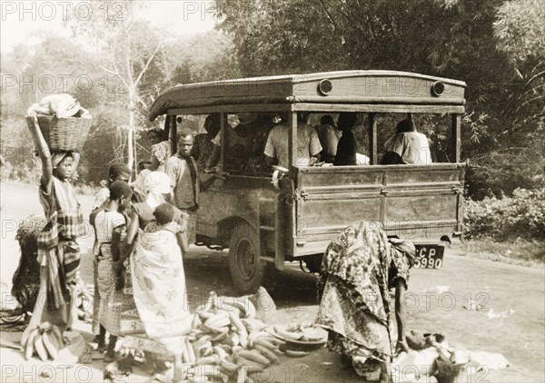 Taxi in the Gold Coast. Plantain sellers and other passengers arrange their loads by the roadside as they prepare to embark in a taxi. Gold Coast (Ghana), circa 1950. Ghana, Western Africa, Africa.