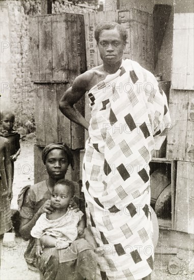An Asante family. An Asante (Ashanti) man stands beside his seated wife and baby, wearing a traditional patterned robe. Asante, Gold Coast (Ghana), circa 1950., Ashanti, Ghana, Western Africa, Africa.