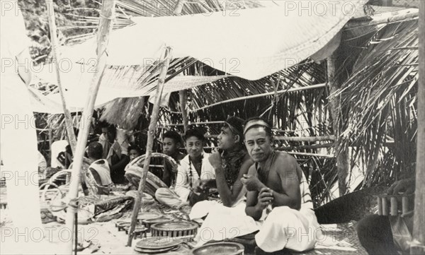 Craft stall at a Fijian market. Fijian craftsmen sit in the shade of canopies as their sell their wares at an outdoor market. Fiji, 1935. Fiji, Pacific Ocean, Oceania.