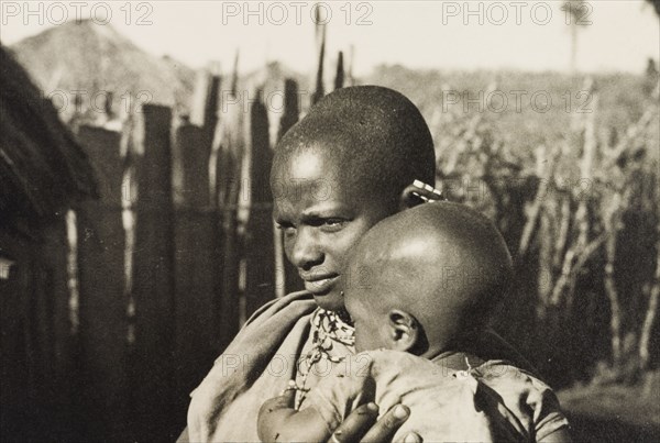 Kikuyu mother and baby. A Kikuyu baby is cradled by its mother, a woman identified in an original caption as "a squatter's wife". Njoro, Kenya, circa 1935. Njoro, Rift Valley, Kenya, Eastern Africa, Africa.