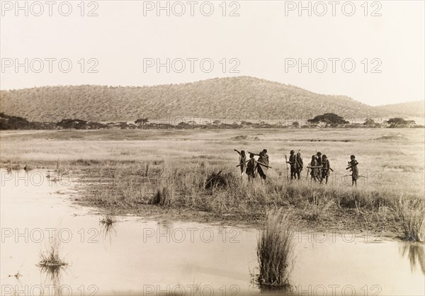 Okiek hunters at Lake Ol Bolossat. A group of Okiek hunters, armed with bows and arrows, search for prey on the shores of Lake Ol Bolossat. Central Kenya, circa 1900., Central (Kenya), Kenya, Eastern Africa, Africa.