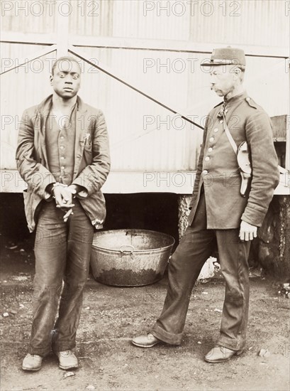 Boer policeman guarding a prisoner. A Boer policeman guards a handcuffed African prisoner during the Second Boer War (1899-1902). The prisoner is labelled in an original caption as a notorious burglar and is described by the racially derogatory term 'kaffir', a word adopted by the Boers to describe black southern Africans. South African Republic (South Africa), circa 1899. South Africa, Southern Africa, Africa.