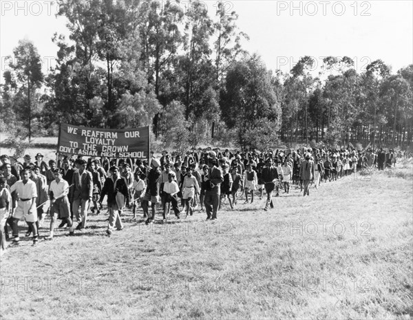 Asian students arrive at Government House. A long line of Asian high school students arrive at Government House to greet Princess Elizabeth and the Duke of Edinburgh during their royal tour of Kenya. They carry a banner, which reads: 'We reaffirm our loyalty to the Crown, Govt. Asian High School'. Nairobi, Kenya, February 1952. Nairobi, Nairobi Area, Kenya, Eastern Africa, Africa.