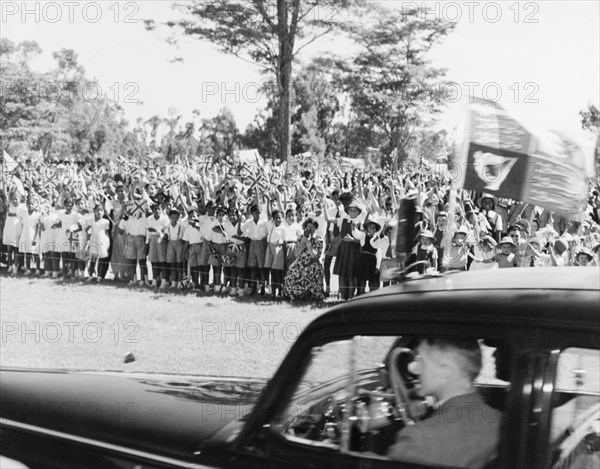 Waving goodbye to Princess Elizabeth. Crowds of schoolchildren wave union jacks flags as a car containing Princess Elizabeth and the Duke of Edinburgh drives past. The royal couple had just left Government House following an official reception to start their royal tour of Kenya. Nairobi, Kenya, February 1952. Nairobi, Nairobi Area, Kenya, Eastern Africa, Africa.