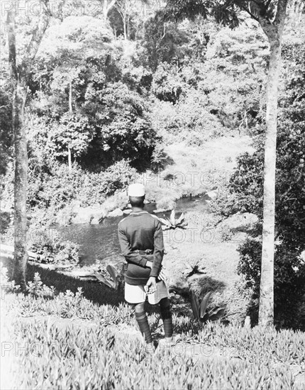 In the gardens of the Royal Lodge, Nyeri. A uniformed man looks out over the Sagana River as it runs through the gardens of Royal Lodge in Nyeri. The lodge was presented to Princess Elizabeth and the Duke of Edinburgh by the people of Kenya in 1952, but was not immediately visited by the royal couple, whose official tour of Kenya was cut unexpectedly short by the death of King George VI on 6 February. Nyeri, Kenya, February 1952. Nairobi, Nairobi Area, Kenya, Eastern Africa, Africa.