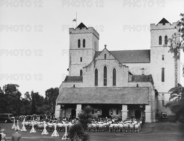 Memorial service for King George VI, Nairobi. A congregation of mourners sit on chairs with their heads bowed outside All Saints Cathedral during a memorial service for King George VI, who died in his sleep at Sandringham House, England, on 6 February 1952. Nairobi, Kenya, circa 6 February 1952. Nairobi, Nairobi Area, Kenya, Eastern Africa, Africa.