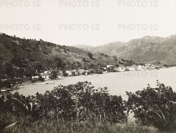 Coastline of Tortola. View along a stretch of coastline on the island of Tortola, where a small settlement borders the Caribbean Sea at the foot of a mountainous slope. Tortola, British Virgin Islands, circa 1931., Tortola, British Virgin Islands, Caribbean, North America .