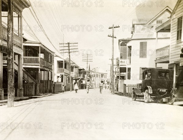 Commercial street in Belize. View down a wide commercial street in Belize City, which is flanked by wooden, balconied buildings and interspersed with tall electricity pylons. Belize City, Belize, 1931. Belize, Belize, Belize, Central America, North America .