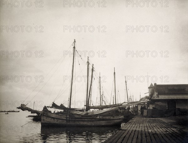 A harbour at Port of Spain. A row of sailing boats is moored to a landing stage at Port of Spain harbour. Port of Spain, Trinidad, circa 1920. Port of Spain, Trinidad and Tobago, Trinidad and Tobago, Caribbean, North America .