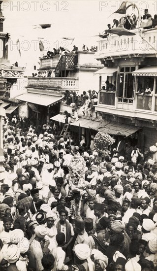 Street festival in Secunderabad. Crowds of people carry religious icons decorated with garlands as they process through a city street during a festival, possibly the Hindu Ganesh Festival (Ganesh Chaturthi). Spectators watch the festivities from nearby rooftops and balconies. Secunderabad (Hyderabad), Andhra Pradesh, India, circa 1930. Hyderabad, Andhra Pradesh, India, Southern Asia, Asia.