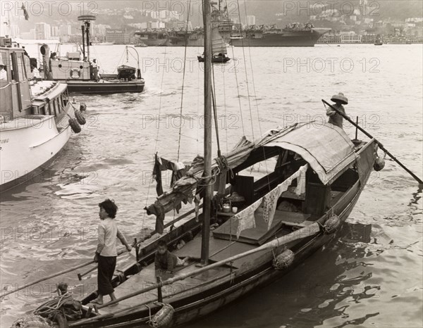 A sampan in Victoria Harbour. A sampan is moored at steps in Victoria Harbour, waiting to ferry passengers from Kowloon to Hong Kong Island. An original caption comments that the sampans faced fierce competition from steamer ferries, which took "only five minutes or so to cross the harbour and (cost) only 10 cents". Kowloon, Hong Kong, China, 1963. Kowloon, Hong Kong, China, People's Republic of, Eastern Asia, Asia.