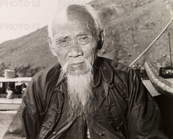 An elderly Chinese fisherman. Portrait of an elderly fisherman sitting on a boat in a Hong Kong harbour. Hong Kong, China, 1963. Hong Kong, Hong Kong, China, People's Republic of, Eastern Asia, Asia.