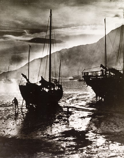 Working against time and tide. A fisherman works against time and tide as he scrapes the barnacles from the underside of his dry-docked fishing junk ready for another fishing trip in the South China Sea. Hong Kong, China, 1963., Hong Kong, China, People's Republic of, Eastern Asia, Asia.