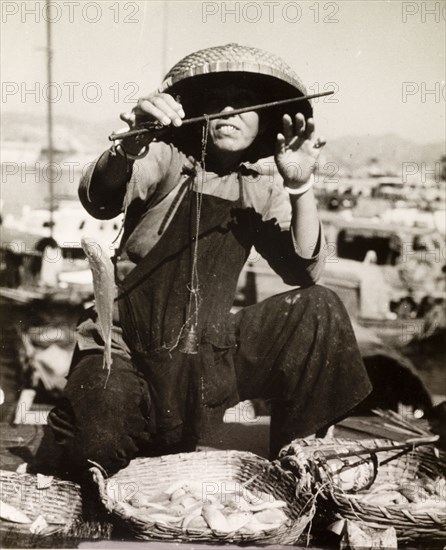 Weighing the day's catch. A fisherman weighs the fish from his day's catch at a harbour in Hong Kong. An original caption comments that "all fish in Hong Kong are sold by weight and not per fish. The old fashioned scales are used by all vendors of foodstuffs'. Hong Kong, China, 1963., Hong Kong, China, People's Republic of, Eastern Asia, Asia.