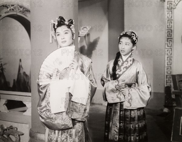 Scene from a Chinese opera. Two Chinese actresses perform in an opera at a Hong Kong theatre. One holds a fan and both wear embroidered silk robes with elaborate hair ornaments. Hong Kong, China, 1963., Hong Kong, China, People's Republic of, Eastern Asia, Asia.