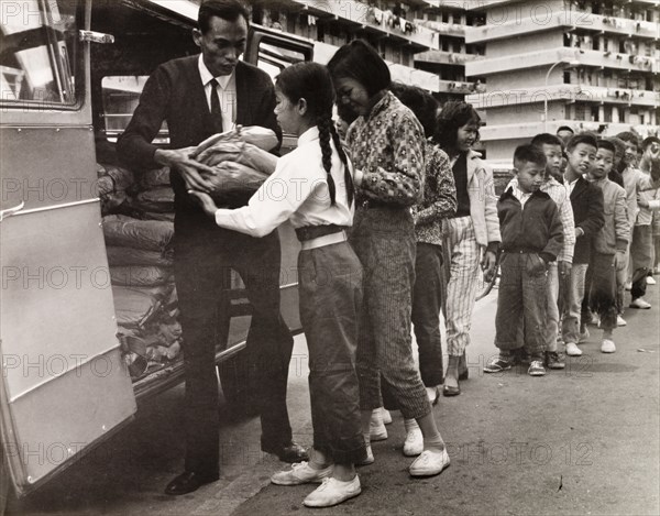 Children queuing for food, Hong Kong. City children queue outside a resettlement block in Kowloon, waiting to receive food parcels from the back of a charity van. Kowloon, Hong Kong, China, 1963. Kowloon, Hong Kong, China, People's Republic of, Eastern Asia, Asia.