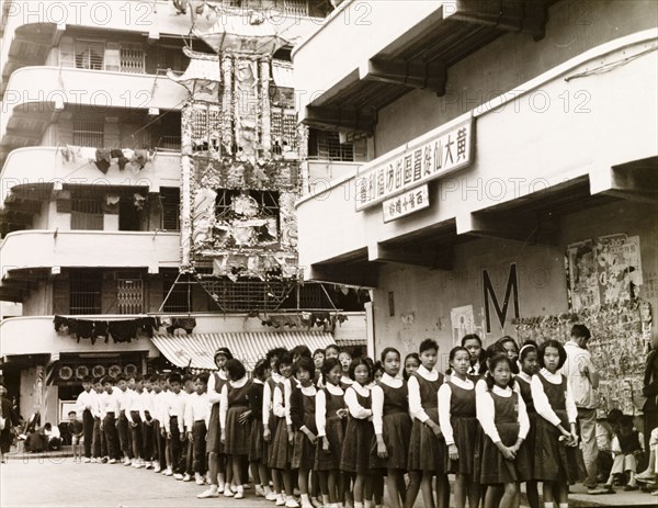 Hong Kong schoolchildren. Uniformed schoolchildren queue in separate lines of boys and girls as they wait to enter their school. An original caption comments that "most school buildings in Hong Kong are used day and night in order to accommodate three different schools". Hong Kong, China, 1963., Hong Kong, China, People's Republic of, Eastern Asia, Asia.