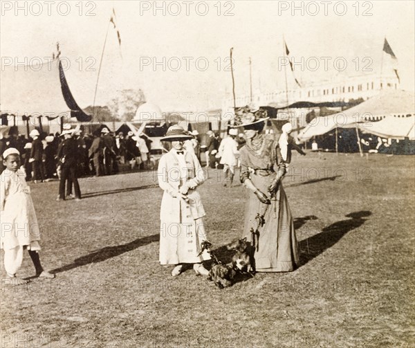 Women attending a dog show, Calcutta. Minnie Murray (left) and a friend, both elegantly dressed and wearing decorated, wide-brimmed hats, hold the leads of two prize-winning dachshunds, Hunden and Piper, at a dog show in Calcutta. Calcutta (Kolkata), India, 1912. Kolkata, West Bengal, India, Southern Asia, Asia.