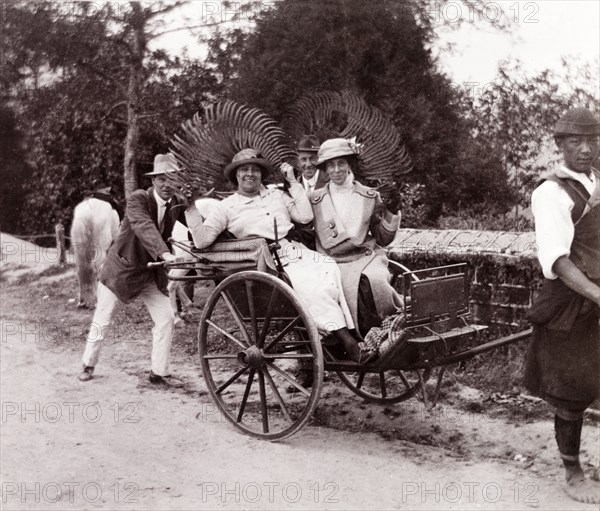 Posing in a rickshaw, Darjeeling. Two British ladies travelling in a rickshaw pose jokingly for the camera holding up fern leaves as headdresses, while two male companions pretend to push the rickshaw from behind. Darjeeling, India, 1916. Darjeeling, West Bengal, India, Southern Asia, Asia.