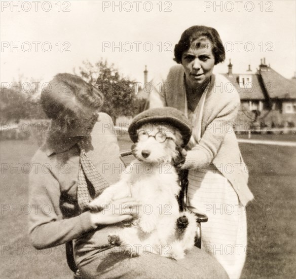 Dressing up the dog. Minnie Murray and her daughter dress up the family's pet dog in a flat cap and glasses, whilst holidaying at the Country Life Hotel in Datchet, near Windsor. Datchet, England, circa 1925., Berkshire, England (United Kingdom), Western Europe, Europe .