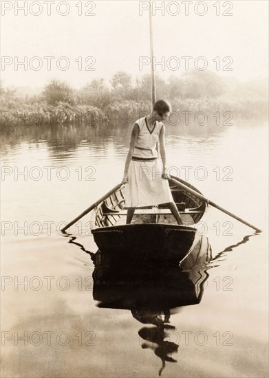 Rowing on the Norfolk Broads. A lady stands alone in a rowing boat on a river in the Norfolk Broads. Norfolk, England, 1930., Norfolk, England (United Kingdom), Western Europe, Europe .