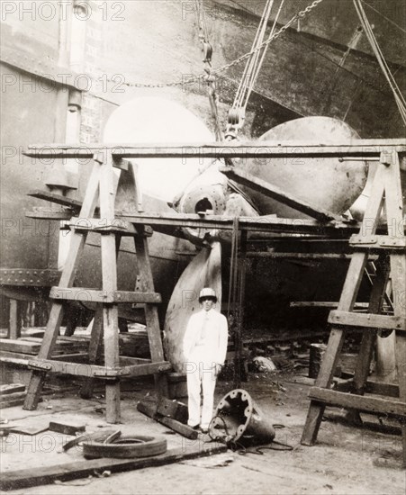 Kidderpore dock, Calcutta. James Murray stands beneath a scaffold, which supports the giant propeller of a dry-docked ship at Kidderpore dock. Murray commented that these "ships look very massive from this unusual angle, and rather threatening propped up by those inadequate looking match sticks". Calcutta (Kolkata), India, 1931. Kolkata, West Bengal, India, Southern Asia, Asia.