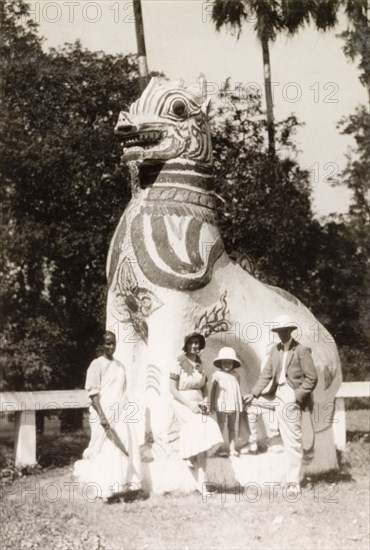Sightseeing at the Shwe Dagon Pagoda. British tourists, accompanied by an Indian ayah (nursemaid), pose beside a large statue outside a temple at the Shwe Dagon Pagoda. Rangoon, Burma (Yangon, Myanmar), 1931. Yangon, Yangon, Burma (Myanmar), South East Asia, Asia.
