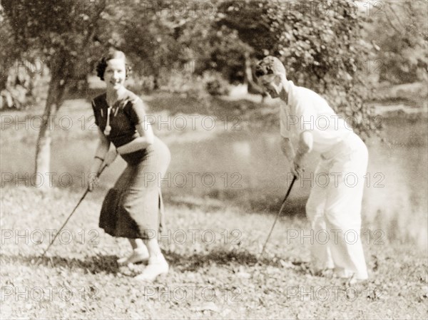 Striking a pose with golf clubs, Calcutta. A European couple strike a pose for the camera holding golf clubs, whilst picnicing in the botanical gardens in Calcutta. Calcutta (Kolkata), India, January 1935. Kolkata, West Bengal, India, Southern Asia, Asia.