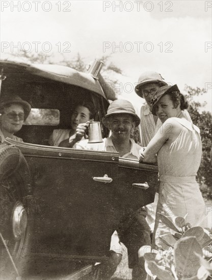 Friends socialising, Calcutta. A group of friends socialise by a motor car, one man raising up a tankard to the camera. Calcutta (Kolkata), India, April 1935. Kolkata, West Bengal, India, Southern Asia, Asia.