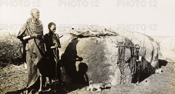 A traditional Maasai hut. A Maasai woman and two children stand beside a traditional Maasai wattle and daub hut in the Sanya Plains. Kilimanjaro, Tanganyika Territory (Tanzania), 21 September 1930., Kilimanjaro, Tanzania, Eastern Africa, Africa.