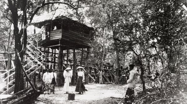 Mr Maduanwella's hut'. Two European women pose in front of 'Mr Maduanwella's hut' at an elephant kraal (enclosure). The stilted hut stands above a stockade into which wild elephants are herded and captured. Ceylon (Sri Lanka), 1912. Sri Lanka, Southern Asia, Asia.