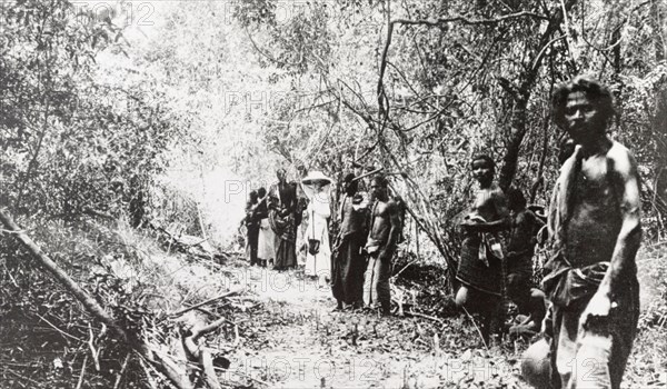 Beaters on an elephant drive, Ceylon. A European woman stands in a jungle clearing with a team of Ceylonian beaters during an elephant kraal or drive. Ceylon (Sri Lanka), 1912. Sri Lanka, Southern Asia, Asia.