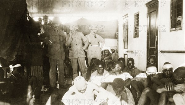 African prisoners of war on a British ship. Indian troops sit and stand behind three British Army officers who discuss a group of African prisoners on the deck of a ship. Related images of the British offensive against German East Africa (Tanzania) during the First World War (1914-18) suggest the men had been captured as prisoners of war. Probably Indian Ocean, circa 1914., Indian Ocean, Africa.
