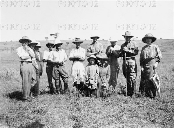 Elspeth, Jos and Nellie Grant at Kitimuru Estate. A group of European landowners pose for an outdoor portrait at Kitimuru Estate, the home of settler farmers Jos (centre, white breeches) and Nellie Grant (kneeling, centre). The Grants arrived in Kenya in 1912 to set up a coffee farm and were joined in 1914 by their seven year old daughter, Elspeth (later Huxley), seen here in the centre. Thika, Kenya, 1914. Thika, Nairobi Area, Kenya, Eastern Africa, Africa.