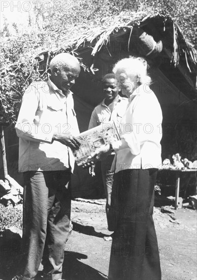 Kamante with Ingrid Lindstrom. Kamante, once head servant and cook for Baroness Karen Blixen, shows his newly published book, 'Longing for Darkness', to Blixen's close friend Ingrid Lindstrom. The book reflects Blixen's (aka Isak Dinesen's) famous novel 'Out of Africa', in which Kamante is a character, but is written from Kamante's point of view and enhanced with drawings and letters. Probably Njoro, Kenya, circa 1975. Njoro, Rift Valley, Kenya, Eastern Africa, Africa.