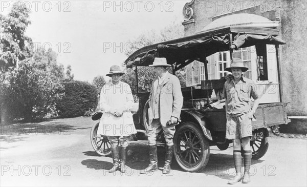 The Grant Family at Kitimura Estate. 14 year old Elspeth Grant (later Huxley) poses for an informal portrait with her settler farmer parents, Jos and Nellie Grant (left). The family stand beside an open-sided car on the driveway of their house at Kitimura Estate. They had arrived in Kenya in 1912 to set up a coffee farm and were joined by Elspeth on New Year's Day 1914. Thika, Kenya, 1921. Thika, Nairobi Area, Kenya, Eastern Africa, Africa.
