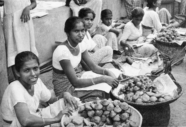 Short-eats' in Ceylon. A row of female traders sit on a city street, selling deep-fried 'short-eats' (snacks) to passers-by. Ceylon (Sri Lanka), circa 1935., Sri Lanka, Southern Asia, Asia.