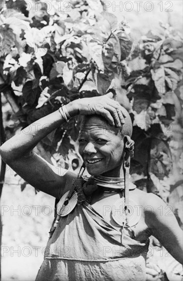 One of Chief Murigo's 19 wives'. Portrait of a Kikuyu woman, wearing several items of jewellery including a pair of heavy, ornate earrings and a necklace. She is identified in an original caption as ?One of Chief Murigo's 19 wives?, her marriage status indicated by her shaven head. South Nyeri, Kenya, 1936. Nyeri, Central (Kenya), Kenya, Eastern Africa, Africa.