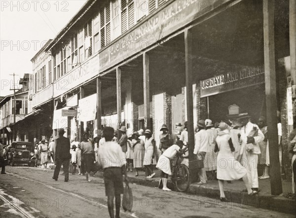 Frederick Street, Port of Spain. Crowds bustle about on Frederick Street outside a row of commercial buildings. Port of Spain, Trinidad, circa 1931. Port of Spain, Trinidad and Tobago, Trinidad and Tobago, Caribbean, North America .