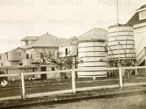 Water butts in a colonial garden, Belize. The rear garden of a colonial house, containing a chicken coup and two large rainwater containers. Belize, 1931. Belize, Central America, North America .