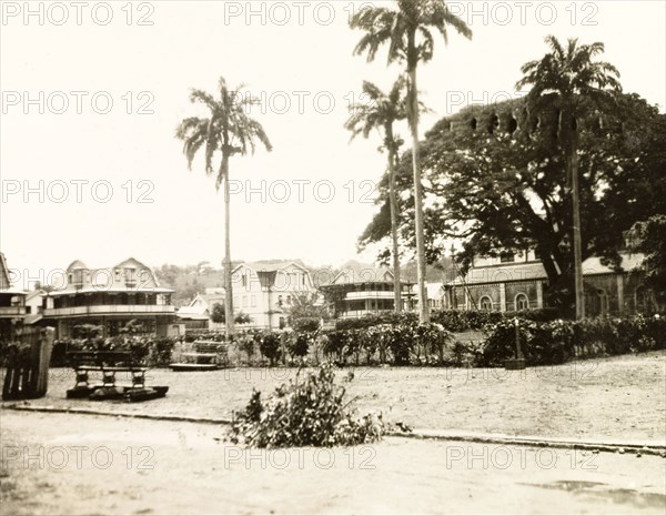 Park benches in St Lucia. Two park benches on a patch of open ground, either a park or garden, are surrounded by colonial-style houses. St Lucia, circa 1931. St Lucia, Caribbean, North America .