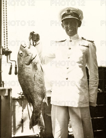 A fish caught on HMS Dauntless. The Captain of HMS Dauntless poses proudly on the ship's deck holding a huge fish that was caught by his crew in the South Atlantic Ocean. South Atlantic Ocean, circa 1931., South Atlantic Ocean, South America .