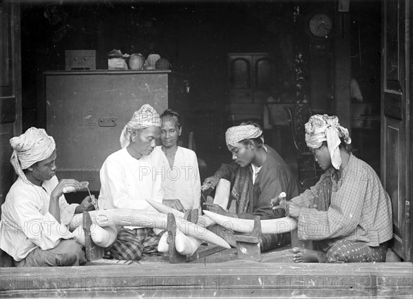 Carving elephant tusks, Burma. Four Burmese men sit on the floor of a workshop carving intricate patterns onto elephant tusks. Burma (Myanmar), circa 1890. Burma (Myanmar), South East Asia, Asia.