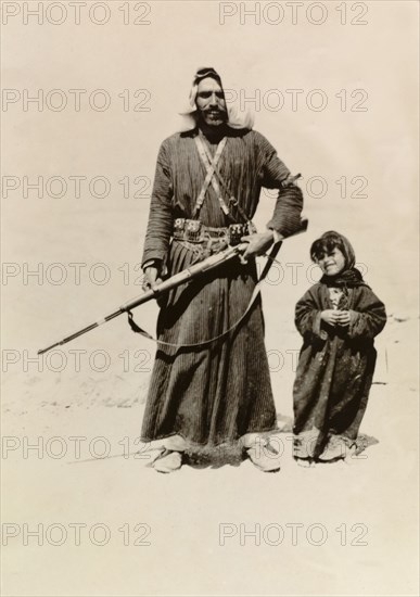 Bedouin father and daughter. Portrait of a bedouin man holding a rifle, who stands in the Palestinian desert accompanied by his young daughter. British Mandate of Palestine (Middle East), circa 1942., Middle East, Asia.