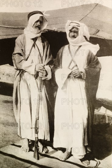 Two bedouin men on watch. Portrait of two bedouin men in traditional dress, one holding a rifle as they stand on watch duty outside their camp site. British Mandate of Palestine (Middle East), circa 1942., Middle East, Asia.