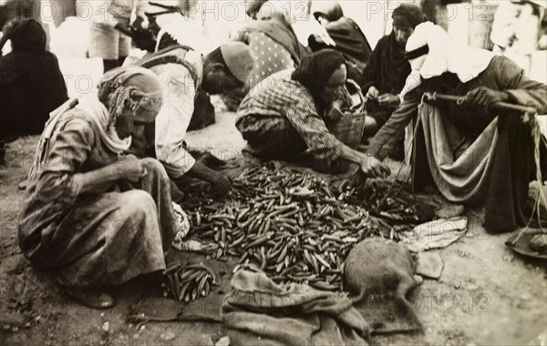 Okra seller, Palestine. Shoppers select okra from a stall at a Palestinian market, which the trader weighs on a set of hand scales. British Mandate of Palestine (Middle East), circa 1942., Middle East, Asia.