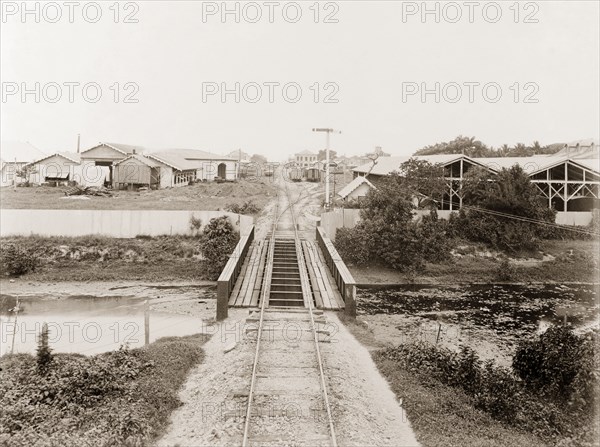 Railway tracks entering Port of Spain. A railway track crosses a river bridge on its approach to the railway terminus at Port of Spain. Port of Spain, Trinidad, circa 1912. Port of Spain, Trinidad and Tobago, Trinidad and Tobago, Caribbean, North America .